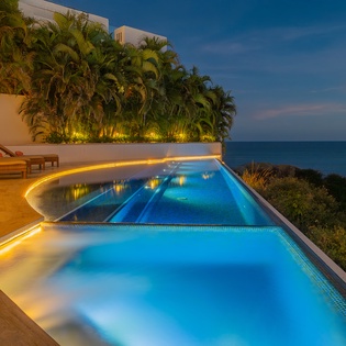Luxurious oceanfront pool with dramatic evening lighting and panoramic sea views creates an unforgettable tropical escape.