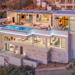 A stunning multi-level modern villa featuring illuminated terraces, infinity pool, and panoramic hillside positioning.