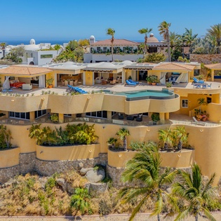 Stunning multi-level villa with curved architecture overlooks tropical coastline, featuring terraced gardens and azure pool amid swaying palms.