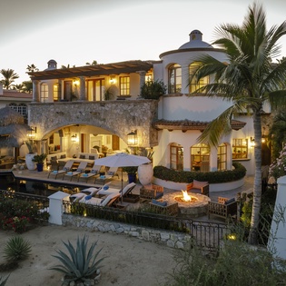 Elegant Mediterranean villa with stone archways, tropical gardens, poolside fire pit, and warm evening lighting creating the perfect luxury retreat.