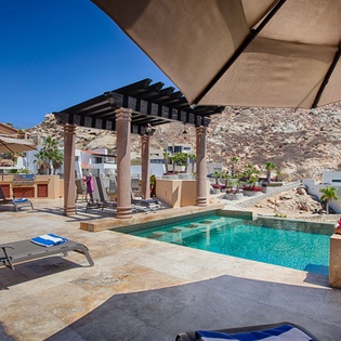 A luxurious hillside retreat where your private pool awaits beneath dramatic desert mountains, complete with loungers, covered pergola, and outdoor kitchen—your perfect sunny escape.