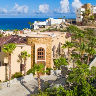 A stunning beachfront villa nestled among palm trees and natural landscaping, with sweeping ocean views and the sparkling Sea of Cortez beyond.