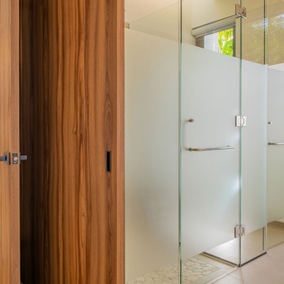Step into your luxurious glass-enclosed shower sanctuary, where modern elegance meets tropical tranquility with garden views beyond.