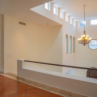 A bright, soaring space where natural light floods through high clerestory windows, creating an airy retreat. The warm terracotta floors add rustic charm to this elegant setting.