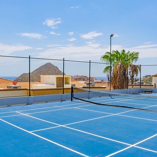 The property features tennis courts with stunning mountain and sea views, surrounded by palm trees and neighborhood rooftops. Courts are equipped with evening lighting for extended play.