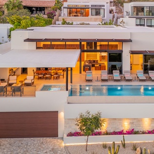 A striking modern villa showcases contemporary architecture with clean lines, illuminated interiors, and a stunning swimming pool set within an upscale hillside neighborhood.