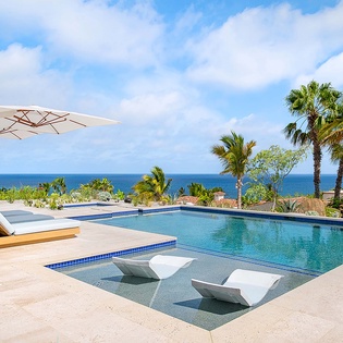 Infinity pool with ocean views and sun loungers—your perfect tropical escape awaits beneath swaying palms and endless blue skies.