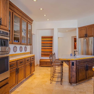Your gourmet kitchen awaits, featuring rich wood cabinetry, a center island with sunny tile countertops, stainless steel appliances, and ample prep space—perfect for cooking and gathering together.