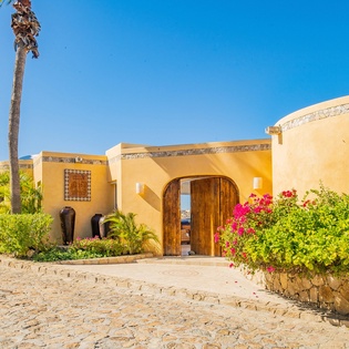 A stunning desert-inspired villa with curved architecture, vibrant bougainvillea, and tropical palms under brilliant blue skies.