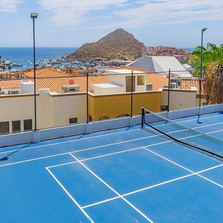 A rooftop tennis court offers stunning coastal views with the sea, marina, and dramatic rock formations visible in the distance—perfect for an active escape in paradise.