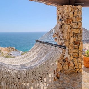 Sway gently in your private hammock while gazing at endless azure waters, surrounded by charming terracotta planters and rustic stone details.