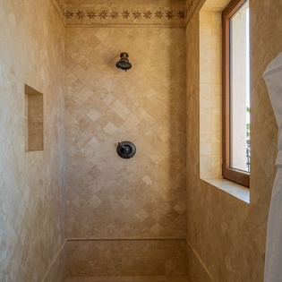 Step into your luxurious travertine shower featuring elegant tile work, dual fixtures, and soft natural light streaming through the window.