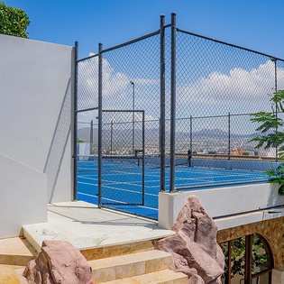 The property features a rooftop tennis court with panoramic mountain and ocean views, surrounded by lush greenery and accessed by beautifully landscaped stone steps.