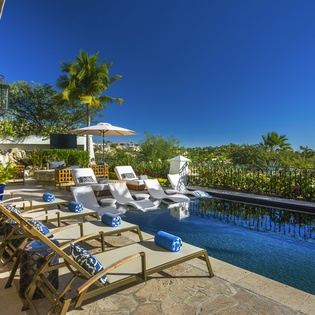 Luxurious infinity pool terrace with premium loungers overlooking lush tropical gardens under endless blue skies.