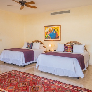 Relax in your spacious room with two comfortable beds, vibrant artwork, and a cooling ceiling fan for perfect comfort.