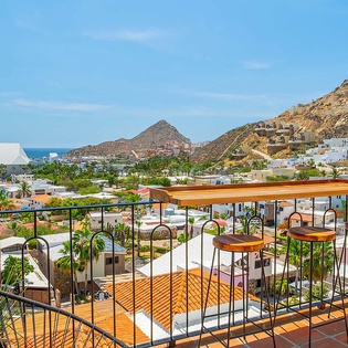 Expansive coastal town views stretch from hillside to sea, with terraced homes cascading toward the waterfront and a cruise ship anchored near the harbor, marking the arrival area.