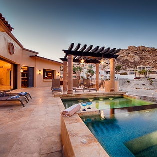The property features a private pool and covered pergola terrace set against dramatic mountain landscapes, captured during the warm golden hour light.