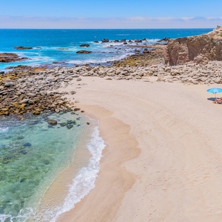 Pristine coastal paradise with crystal-clear waters, rocky tide pools, and golden sand stretches along the shoreline near charming beachfront buildings.