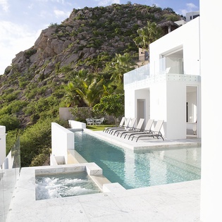 Stunning modern villa with infinity pool and hot tub set against dramatic hillside backdrop.