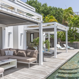 Your private poolside terrace invites you to lounge under a pergola surrounded by lush tropical palms and modern outdoor seating.