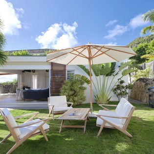 Unwind in your private tropical garden with comfortable lounge chairs under a stylish umbrella, surrounded by lush palms and vibrant greenery.