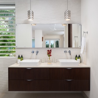 Start your mornings in this elegant dual-vanity bathroom featuring modern pendant lighting, luxurious amenities, and tropical garden views through louvered windows.
