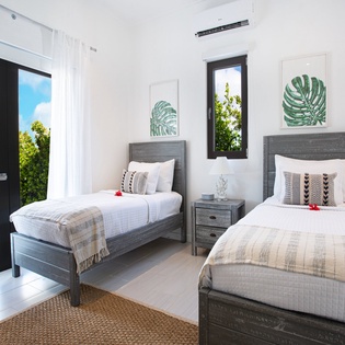 You'll rest peacefully in this bright twin bedroom with crisp linens, tropical art, and natural light streaming through the windows. The air conditioning keeps you comfortable all day.