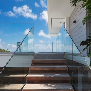 Modern glass staircase with ocean views and tropical landscaping at luxury property entrance.