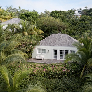 Charming white cottage nestled among lush tropical palms and vibrant flowering gardens in a serene island setting.