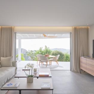 Relax in your spacious living room where floor-to-ceiling windows frame stunning mountain views, creating a seamless flow to your private terrace.