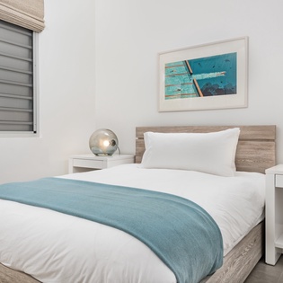 Rest peacefully in your comfortable bedroom with coastal artwork and modern lighting creating a serene atmosphere.