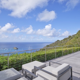 Panoramic ocean views from this stunning hillside deck, where modern lounge seating overlooks crystal-blue waters dotted with sailboats.