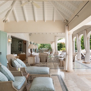 Settle into plush seating beneath soaring white beams and flowing curtains, where soft sea breezes and garden views invite you to unwind in elegant comfort.