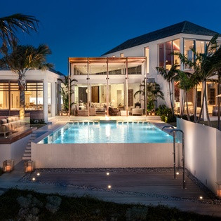 Stunning modern villa with illuminated pool surrounded by swaying palms creates the perfect tropical evening retreat.