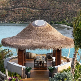 Tropical pavilion with thatched roof overlooking turquoise waters and lush hillsides creates an idyllic Caribbean setting.