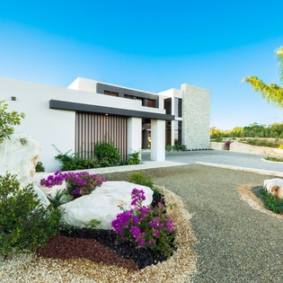 Modern architectural entrance set in lush tropical landscaping with swaying palms and vibrant bougainvillea, welcoming visitors to this contemporary retreat.