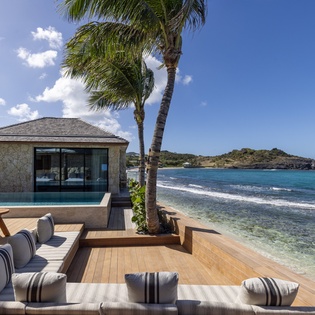 Beachfront villa with infinity pool, palm trees, and pristine ocean waters just steps from the shore.