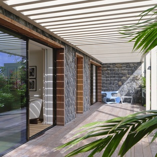 Step onto your private terrace where tropical palms frame elegant stone walls and wooden shutters create perfect indoor-outdoor flow.