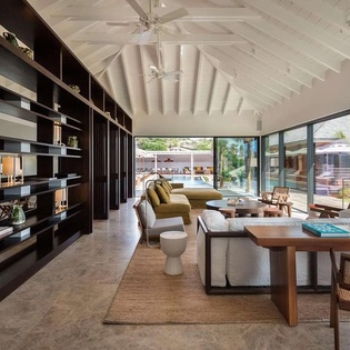 Sink into modern comfort in this airy living space, where soaring ceilings, custom shelving, and floor-to-ceiling glass open your view to the pool and tropical gardens beyond.