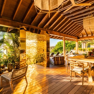 Gather around this stunning handcrafted wooden table under soaring beamed ceilings, surrounded by lush tropical greenery and warm natural light filtering through open-air walls. Your perfect blend of indoor comfort and outdoor serenity.