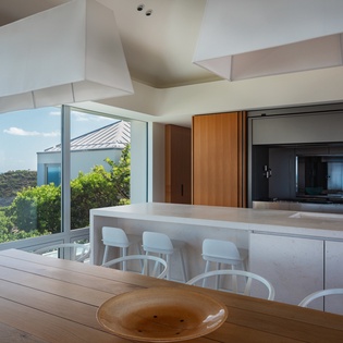 Your modern kitchen flows seamlessly into dining space, framing stunning ocean views through floor-to-ceiling windows.