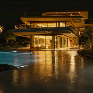 Modern luxury villa showcasing contemporary architecture with illuminated pool and tropical landscaping during evening hours.