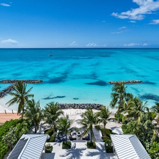 Beachfront property featuring direct access to pristine turquoise waters, sandy shore, and tropical landscaping with palm trees along the coastline.