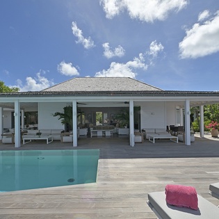 Modern villa with open-air design featuring pristine pool, spacious covered terraces, and tropical gardens under Caribbean skies.
