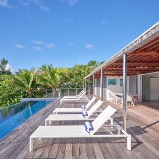 Luxurious infinity pool and sun loungers on private wooden deck surrounded by tropical palms and blue skies.
