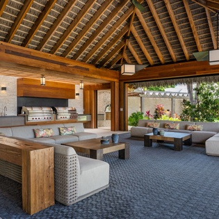 An elegant open-air pavilion featuring a fully equipped outdoor kitchen with built-in grills and comfortable lounge seating surrounded by lush tropical plants.