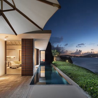 Sleek infinity pool and deck overlook serene waters and distant hills at twilight, creating a peaceful escape for your evening relaxation.