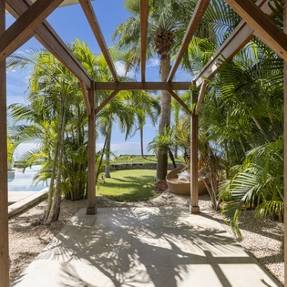 Step into your private tropical oasis where wooden beams frame swaying palms and endless blue skies above your personal paradise.