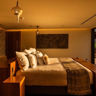 A serene sanctuary bathed in warm golden light, where Moroccan-inspired fixtures cast intricate patterns above your plush bed. Through sliding doors, your private terrace beckons with coastal breezes and relaxation.