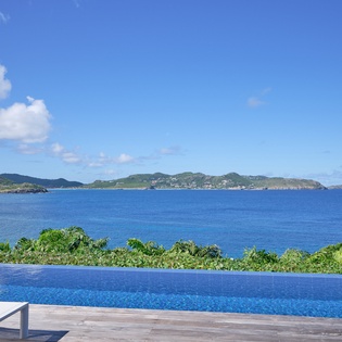 Stunning infinity pool blends seamlessly with crystal-blue Caribbean waters and lush tropical islands beyond.